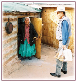 Native American Elder opening door of traditional home to accept supplies.